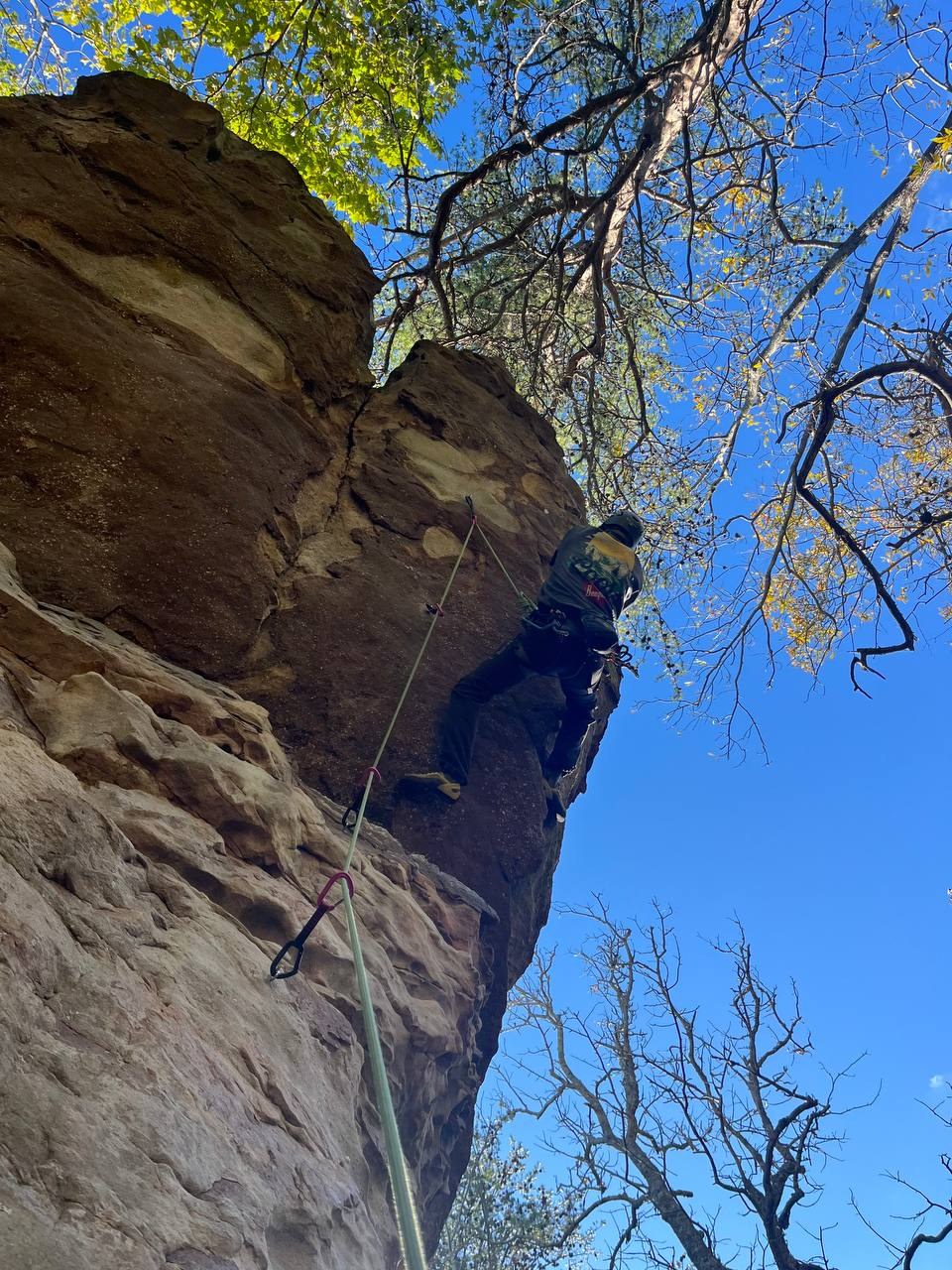Climber working up a steep overhanging sandstone face, rope and quickdraws in the foreground