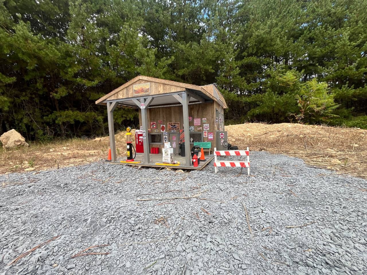 The Sandcreek Service Station — a vintage gas station kiosk ringed by pines